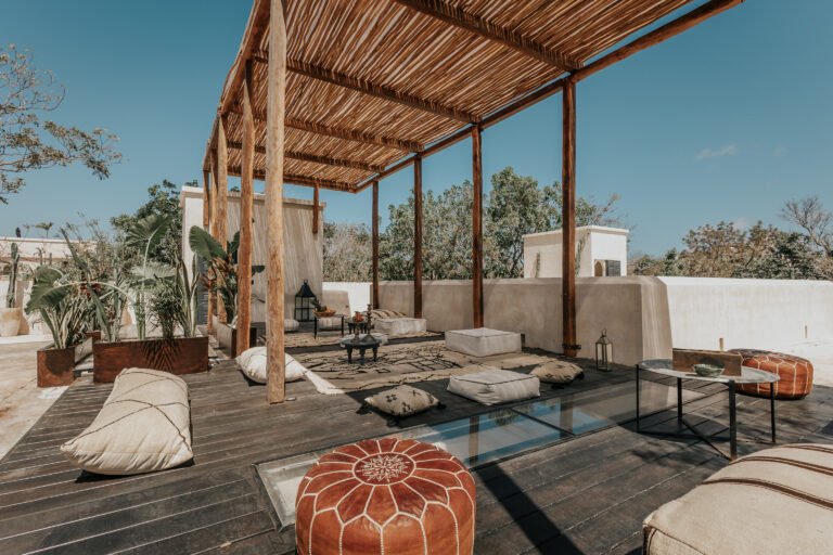 Shaded rooftop terrace with palapa roof, floor cushions and jungle canopy under a clear blue sky at a villa in Tulum