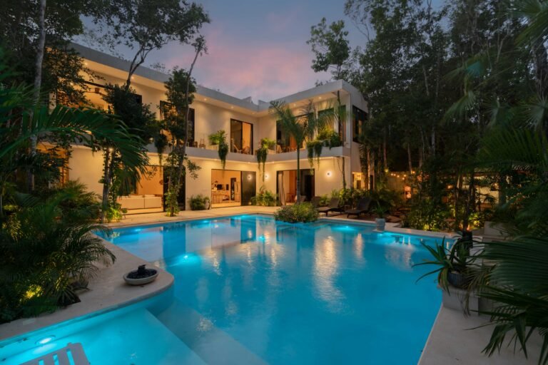 Casa ChenXen at dusk with its illuminated pool, two-storey white facade and surrounding jungle trees in Tulum
