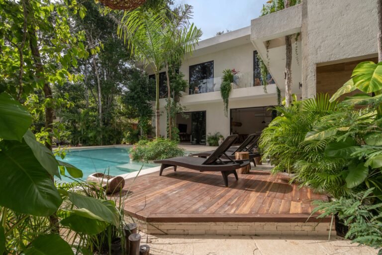 Wooden pool deck with two sun loungers beside the private pool, tropical plants and the two-storey villa at Casa ChenXen
