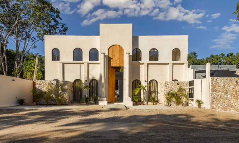 White two-story facade of Casa Alba villa in Tulum with arched windows, a tall wooden entrance door, columns and stone walls