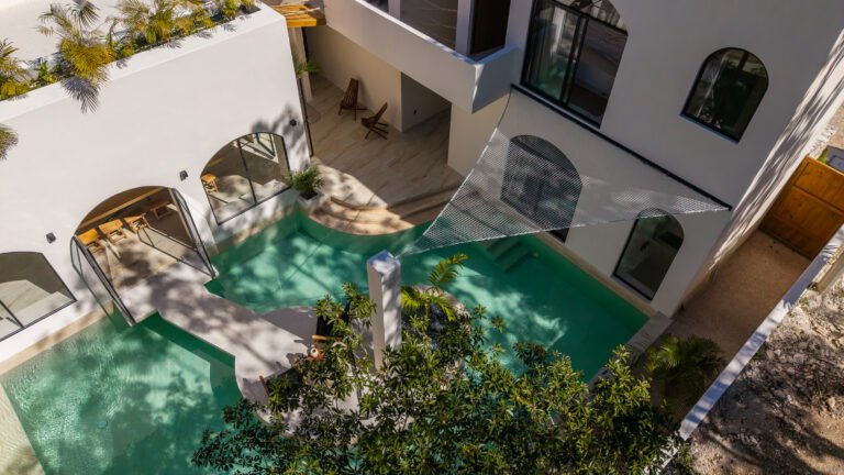 Aerial view of a private villa in Tulum with a turquoise pool, arched terraces and palms, seen from directly above