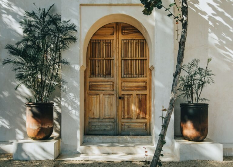 Arched wooden double doors and potted palms at the entrance of a private villa in Tulum, Mexico